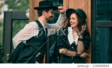 Man tipping hat while smiling at woman in retro outfit 128989684