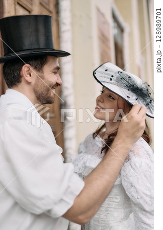 Smiling man in top hat gently lifting woman lace hat outdoors 128989701