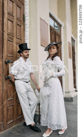 Man in top hat leaning on wooden door beside woman in vintage white dress 128989706