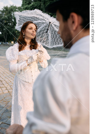 Woman in lace vintage dress with umbrella looking at man out of frame 128989713
