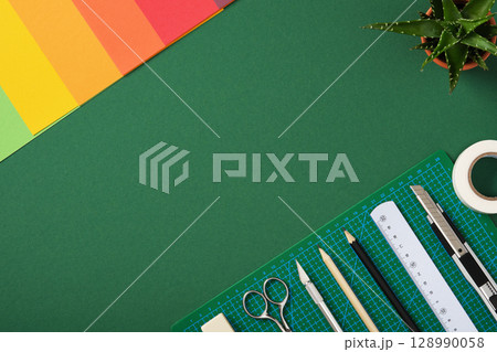 Top view of the paper crafts work table. Stationery supplies and colorful paper arranged on a green background with copy space. 128990058