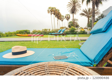 A blue lounge chair with a straw hat on it and a cell phone on it A blue lounge chair with a straw hat on it and a cell phone on it 128990486