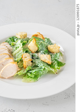 Classic Caesar salad topped with chicken breast served on clean white plate 128991875