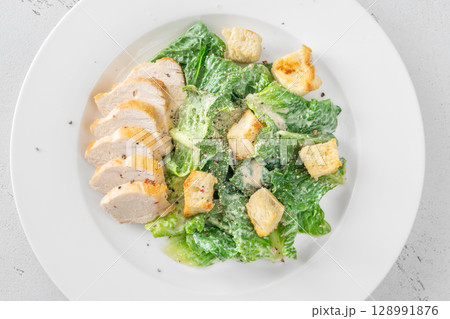 Classic Caesar salad topped with chicken breast served on clean white plate 128991876