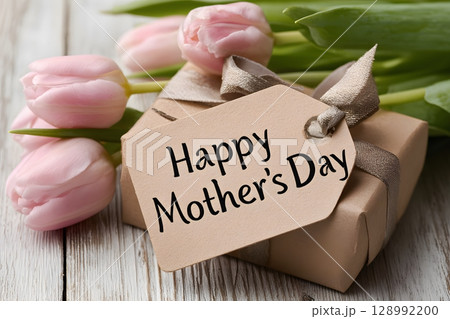 A lovely gift box with a happy mother's day tag is beautifully displayed alongside fresh pink tulips on rustic wood, perfect for celebration. 128992200