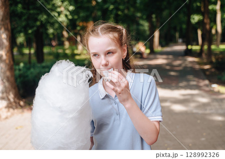 A joyful girl in a park happily eating cotton candy, capturing a moment of childhood delight and outdoor fun A joyful girl in a park happily eating cotton candy, capturing a moment of childhood delight and outdoor fun 128992326