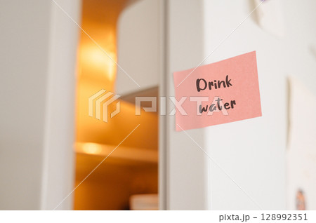 Drink Water reminder sticker prominently placed on a refrigerator, promoting hydration  128992351