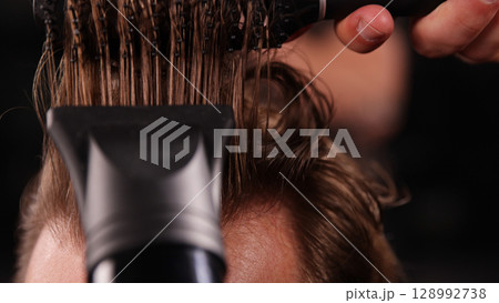 Young Man with Beard at Barber Shop. Barber is Preparing his Haircut. Dark Atmosphere, Black Background. Concept of Barber and a Client. 128992738
