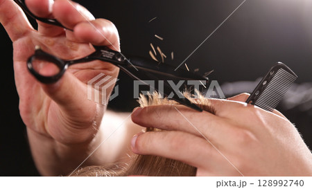 Young Man with Beard at Barber Shop. Barber is Preparing his Haircut. Dark Atmosphere, Black Background. Concept of Barber and a Client. 128992740