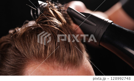 Young Man with Beard at Barber Shop. Barber is Preparing his Haircut. Dark Atmosphere, Black Background. Concept of Barber and a Client. Young Man with Beard at Barber Shop. Barber is Preparing his Haircut. Dark Atmosphere, Black Background. Concept of Barber and a Client. 128992748