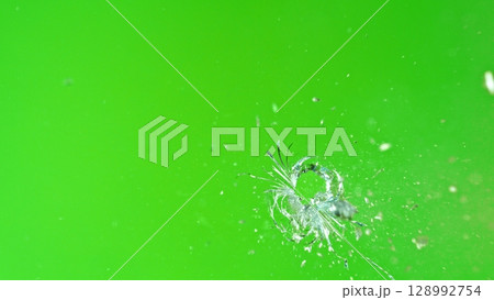 Close-up of gunshot through the glass, shattering against the green background 128992754