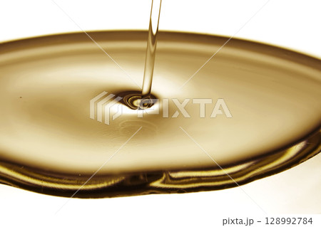 Pouring oil in golden tones. The texture of a cosmetic or other oil product. Pouring oil in golden tones. The texture of a cosmetic or other oil product. 128992784
