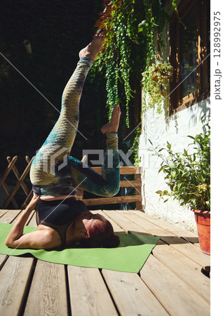 Woman Practicing Outdoor Yoga in Shoulderstand Pose on Sunny Patio Woman Practicing Outdoor Yoga in Shoulderstand Pose on Sunny Patio 128992975