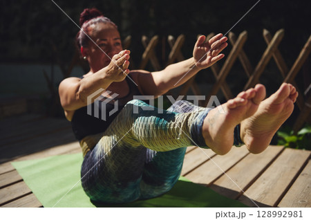 Woman Practicing Yoga Outdoors Sitting on a Mat in a Challenging Pose Woman Practicing Yoga Outdoors Sitting on a Mat in a Challenging Pose 128992981