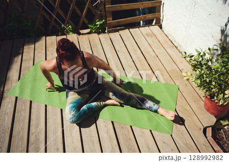 Woman Practicing Outdoor Yoga on a Wooden Deck with Green Mat Woman Practicing Outdoor Yoga on a Wooden Deck with Green Mat 128992982