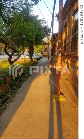 Sunlit Urban Sidewalk with Old Brick Building and Long Shadows 128993542