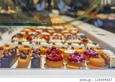 Showcase with cakes and desserts. Colorful assortment of gourmet cakes and pastries displayed in bakery showcase with elegant detail. Concept of desserts, patisserie art, sweet temptation Showcase with cakes and desserts. Colorful assortment of gourmet cakes and pastries displayed in bakery showcase with elegant detail. Concept of desserts, patisserie art, sweet temptation 128994887