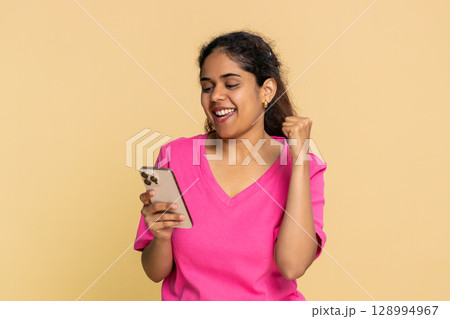 Indian woman happily looking smartphone screen, jumping joyfully, celebrating great online news Indian woman happily looking smartphone screen, jumping joyfully, celebrating great online news 128994967