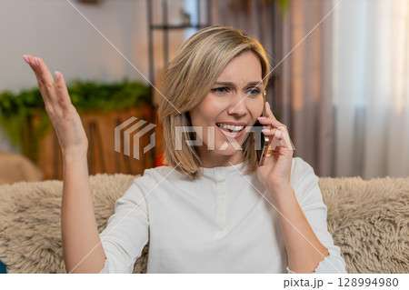Adult woman arguing on smartphone at home, waving hands nervously with anger and expressive emotion 128994980