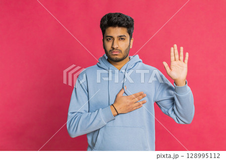 Indian man raising hand to take oath, promising to be honest and to tell truth keeping hand on chest 128995112