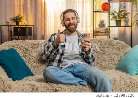 Young man in wireless headphones at home, groove, music listen, thumbs up, cool track, relaxed vibe 128995120