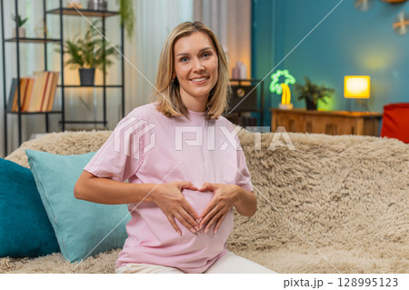 Pregnant woman forming heart with hands over belly smiling enjoying sweet loving moment before birth Pregnant woman forming heart with hands over belly smiling enjoying sweet loving moment before birth 128995123