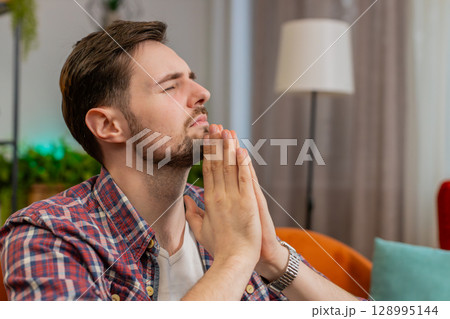 Tensed young man folding palms together pray to God ask for help feel stressed looks desperate 128995144