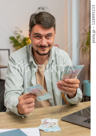 Rich happy Caucasian man counting money cash using laptop calculate domestic bills at home table 128995215