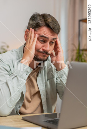 Angry furious man freelancer using laptop working at home office having nervous breakdown at work 128995269