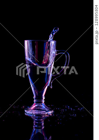 Still life with a glass beaker with splashed liquid on a black background 128995804