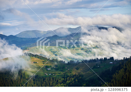 Picturesque scene of mountain valley blanketed in mist, with patches of green pastures and scattered houses. Clouds drift gently over forested hills, creating serene and tranquil atmosphere. Picturesque scene of mountain valley blanketed in mist, with patches of green pastures and scattered houses. Clouds drift gently over forested hills, creating serene and tranquil atmosphere. 128996375