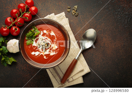 Tomato soup with cream, pumpkin seeds and herbs on brown background top view, copy space 128996580
