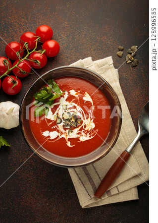 Tomato soup with cream, pumpkin seeds and herbs on brown background top view Tomato soup with cream, pumpkin seeds and herbs on brown background top view 128996585