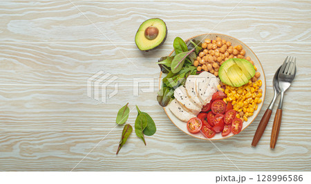 Healthy bowl with chicken breast, avocado, chickpeas, corn and tomatoes on white wooden table top view. Diet and healthy food concept Healthy bowl with chicken breast, avocado, chickpeas, corn and tomatoes on white wooden table top view. Diet and healthy food concept 128996586