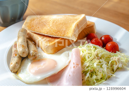 洋風の朝食セット、トーストと目玉焼き、ソーセージやサラダ添え 洋風の朝食セット、トーストと目玉焼き、ソーセージやサラダ添え 128996604
