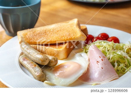 洋風の朝食セット、トーストと目玉焼き、ソーセージやサラダ添え 128996606