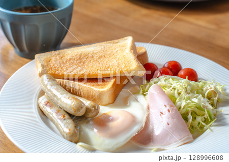 洋風の朝食セット、トーストと目玉焼き、ソーセージやサラダ添え 128996608
