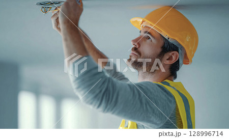 Electrician on Ladder Installing Ceiling Light Fixture in Bright Interior Electrician on Ladder Installing Ceiling Light Fixture in Bright Interior 128996714