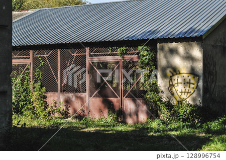 Old Abandoned Rusty Warehouse Buildings Amidst Greenery and Sunlight 128996754