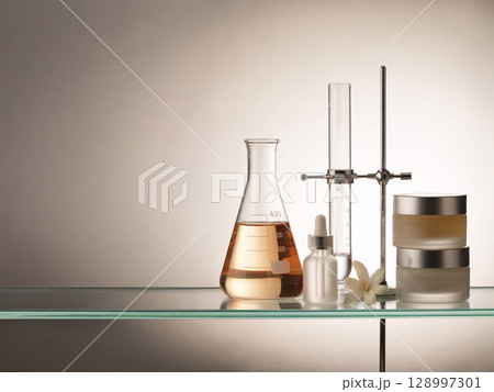 Glass skincare jars and serum dropper with lab beaker and blossom on clear shelf, combining scientific precision and natural elegance 128997301
