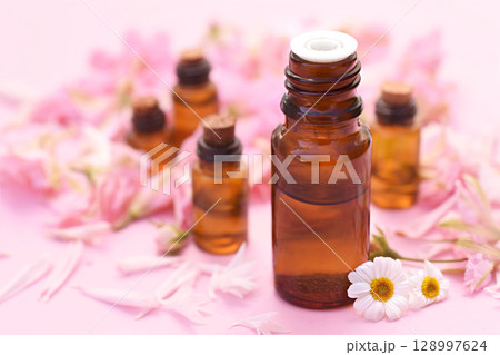 Essential oil bottles on pink flowers background, selective focus, shallow DOF 128997624
