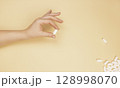 A white pill in a woman's hand on a beige background. The concept of first aid. 128998070