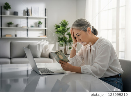金銭的損失に目を覆い悲しむ高齢女性：パソコンと向き合う絶望 128999210