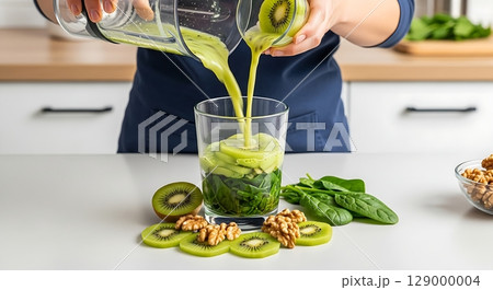 Pouring a Vibrant Green Smoothie into a Glass Layered with Fresh Kiwi and Spinach. 129000004