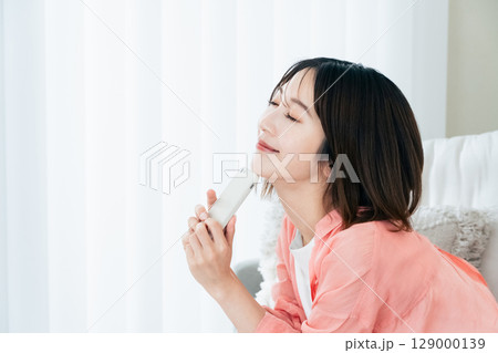 ソファでスマホを見る若い女性 ソファでスマホを見る若い女性 129000139