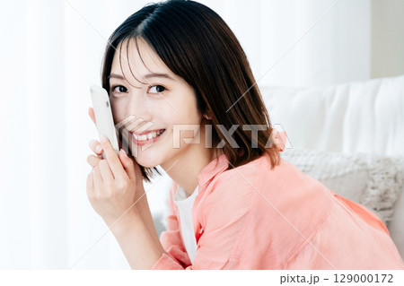 ソファでスマホを見る若い女性 ソファでスマホを見る若い女性 129000172