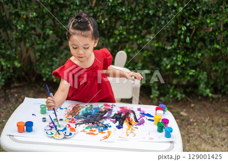happy toddler girl painting watercolor in paper at backyard. happy toddler girl painting watercolor in paper at backyard. 129001425