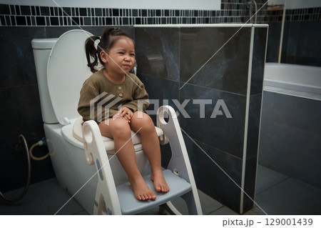 toddler girl sitting on toilet at home and suffering from stomachache and constipation 129001439