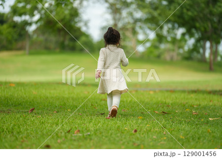 toddle girl in white dress walking on green grass field toddle girl in white dress walking on green grass field 129001456