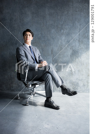 グレーバックで椅子に座るスーツのビジネスマン全身 グレーバックで椅子に座るスーツのビジネスマン全身 129001791
